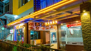Un restaurante muy iluminado con fachada de vidrio, mesas al aire libre y un letrero que indica Hotel Dream Palace.