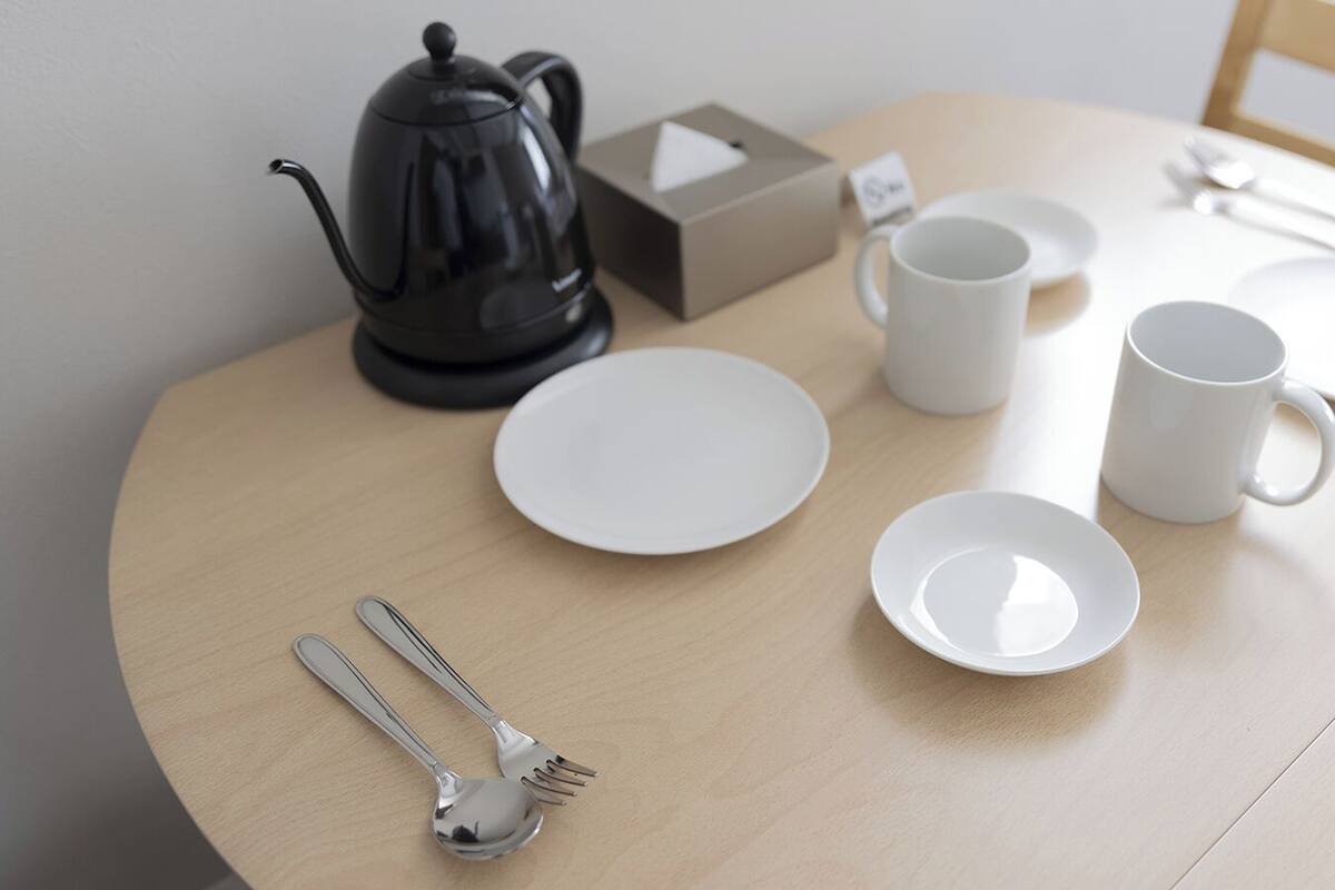 Ein runder Holztisch mit einer schwarzen Teekanne, weißen Tellern, einer weißen Tasse sowie Besteck.