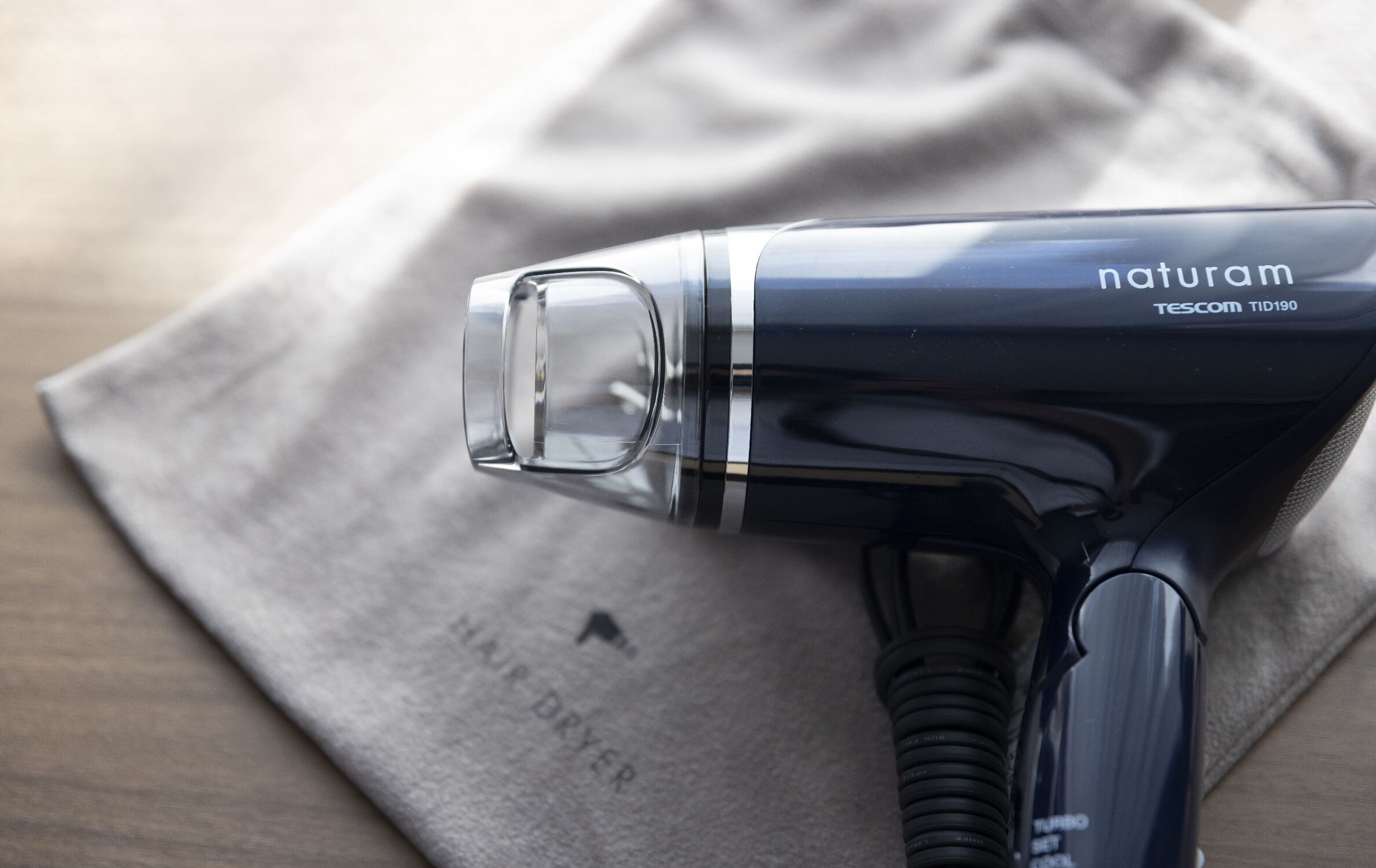 A hair dryer with a clear nozzle, placed on a grey cloth.