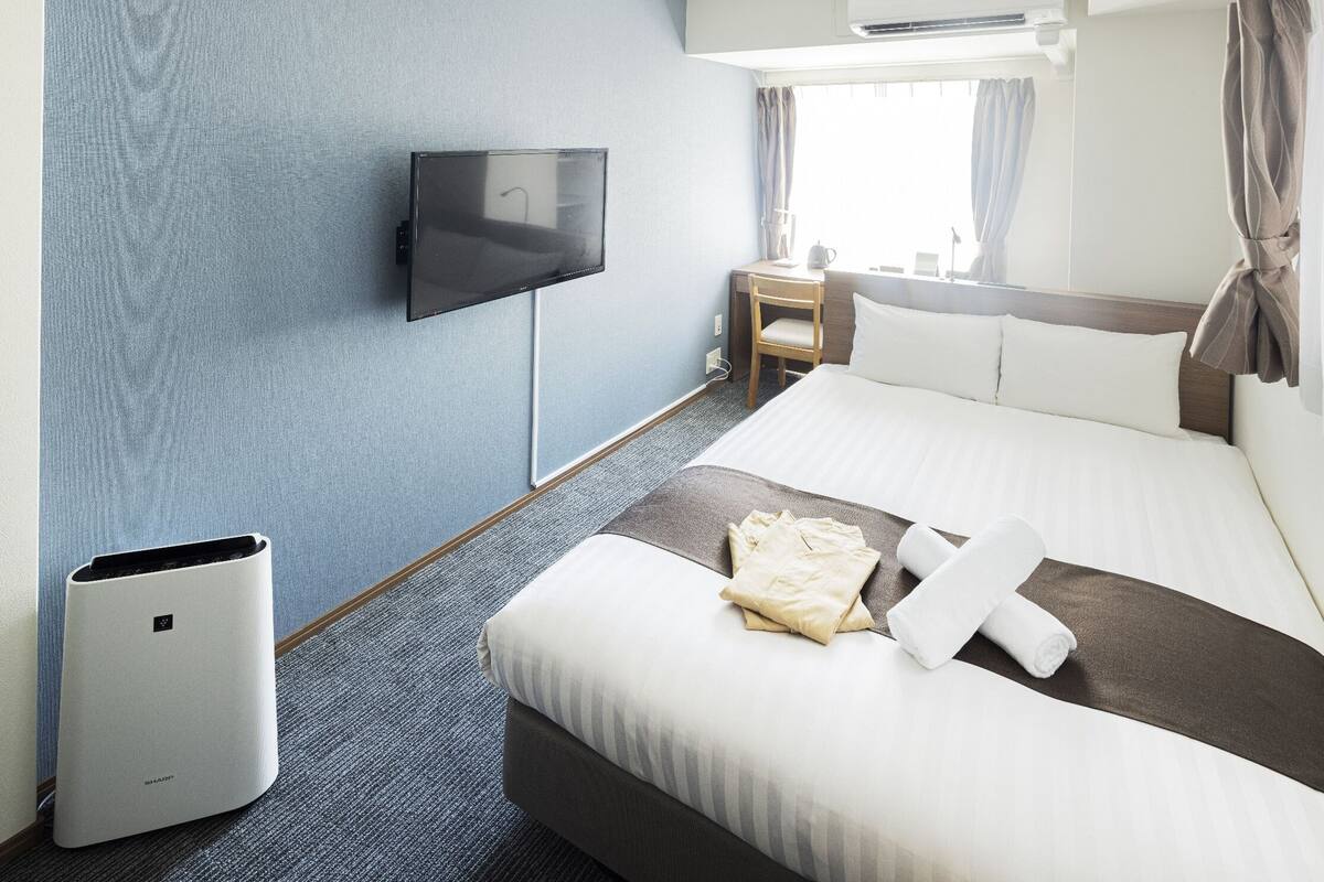 Ein Hotelzimmer mit Bett, Schreibtisch, Sessel, Fernseher und einem Fenster mit Vorhängen.
