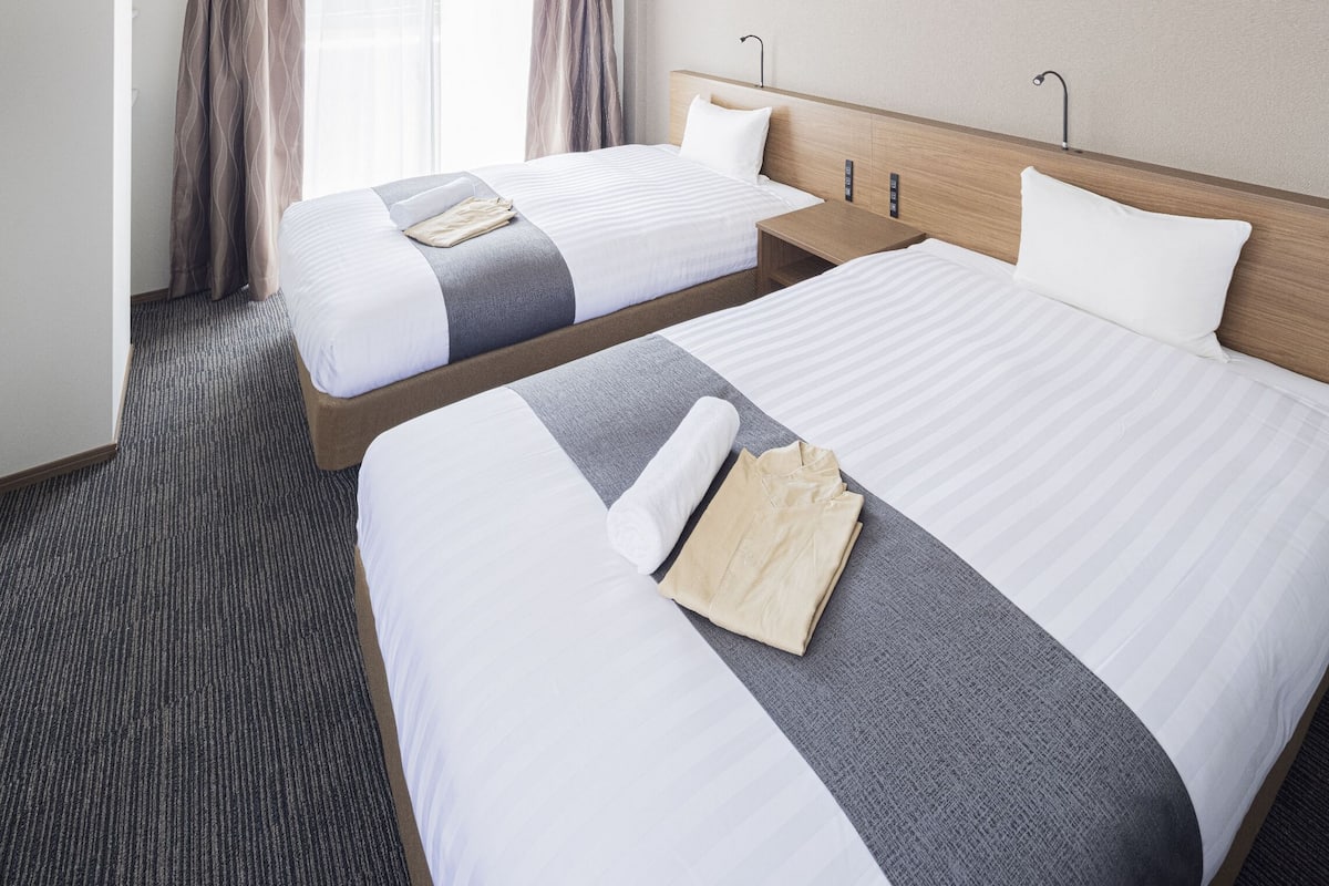 Ein Hotelzimmer mit zwei Betten, einem Holzkopfende, einem kleinen Nachttisch und Teppichboden.