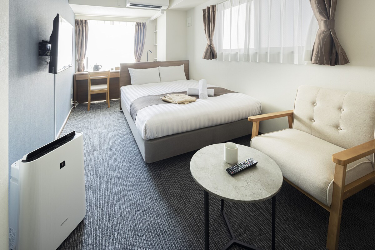 A hotel room with a bed, a chair, a small table, a desk, and a television.