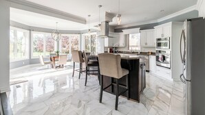 A spacious kitchen with a large island, white cabinetry, and a stainless steel refrigerator.