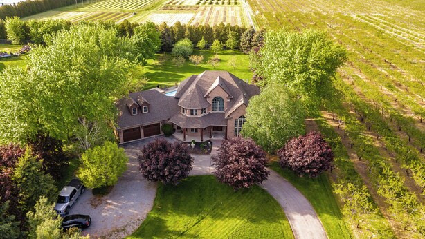 A large, two-story house with a garage, surrounded by lush greenery and a well-maintained lawn.