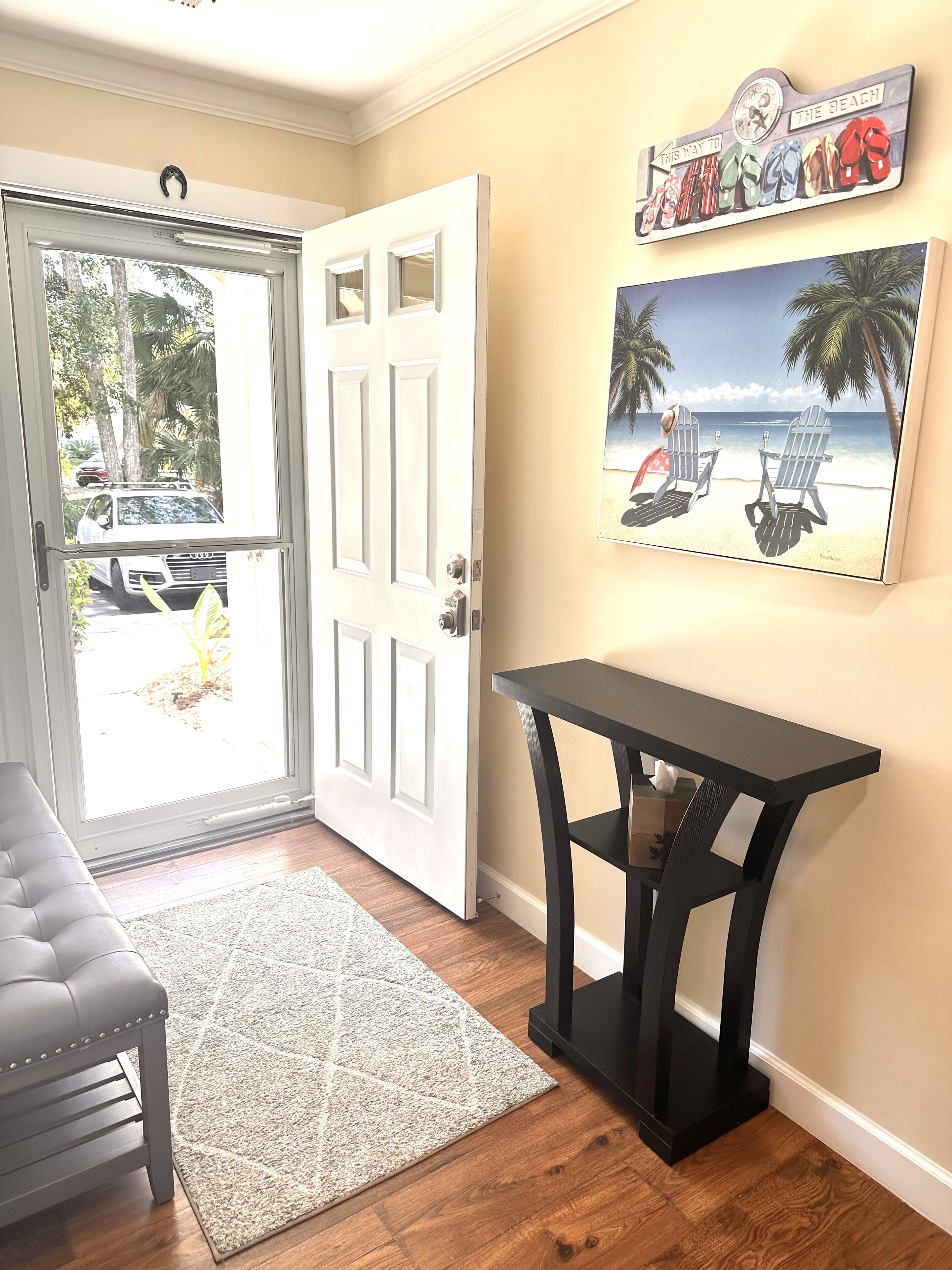 Une pièce avec une porte blanche, une table noire et un tableau sur le mur représentant un paysage de plage.