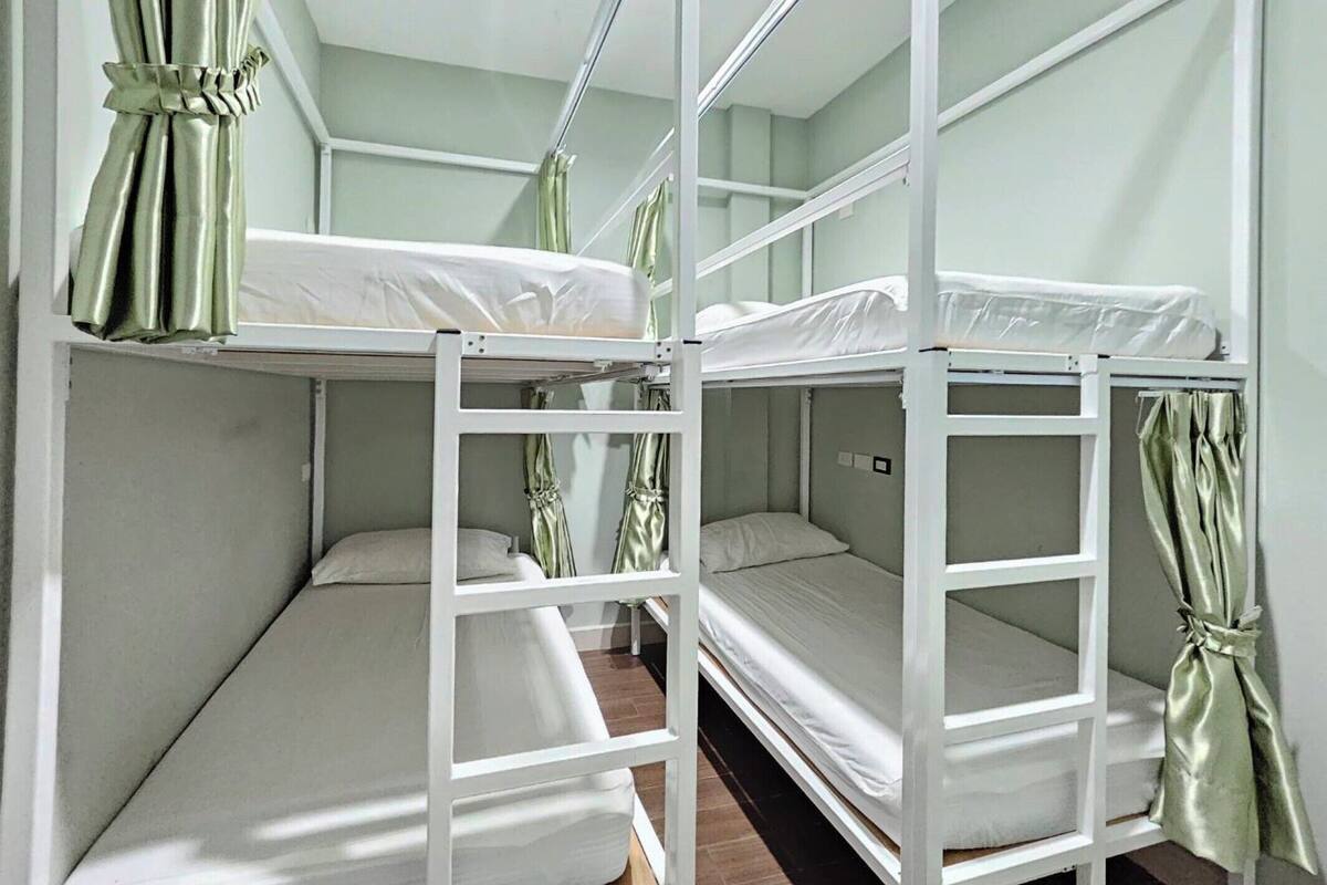 Een slaapkamer met stapelbedden, witte metalen frames en groene gordijnen.