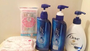 Ein Badezimmerschrank mit verschiedenen Pflegeprodukten, darunter eine Flasche Dove Lotion, zwei Flaschen H&S Duschgel, ein pinkfarbenes Gesichtsreinigungs Produkt und eine Taschentuchbox.