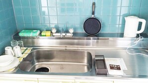 Eine Küche mit Spüle aus Edelstahl, einer Bratpfanne, einem Wasserkocher und verschiedenen Küchenutensilien.