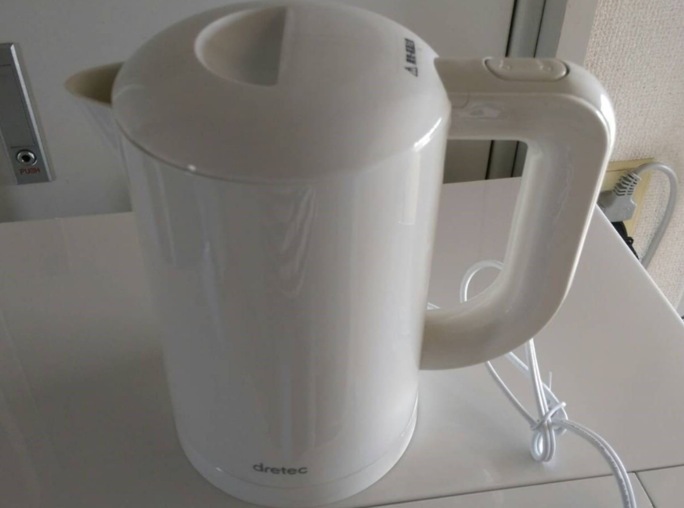 A white electric kettle with a handle and cord on a white surface.