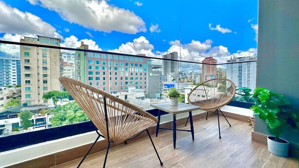 A balcony with two wicker chairs, a small table, and a potted plant. - Stunning City Center Condo Full AC, Pool, Near All (Santo Domingo)