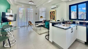 A modern living room with a TV, seating, and a kitchen area with a sink and counter. - Stunning City Center Condo Full AC, Pool, Near All (Santo Domingo)