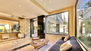 A modern living room with a large window, a sofa, a coffee table, and a seating area with a plant. - Stunning City Center Condo Full AC, Pool, Near All (Santo Domingo)
