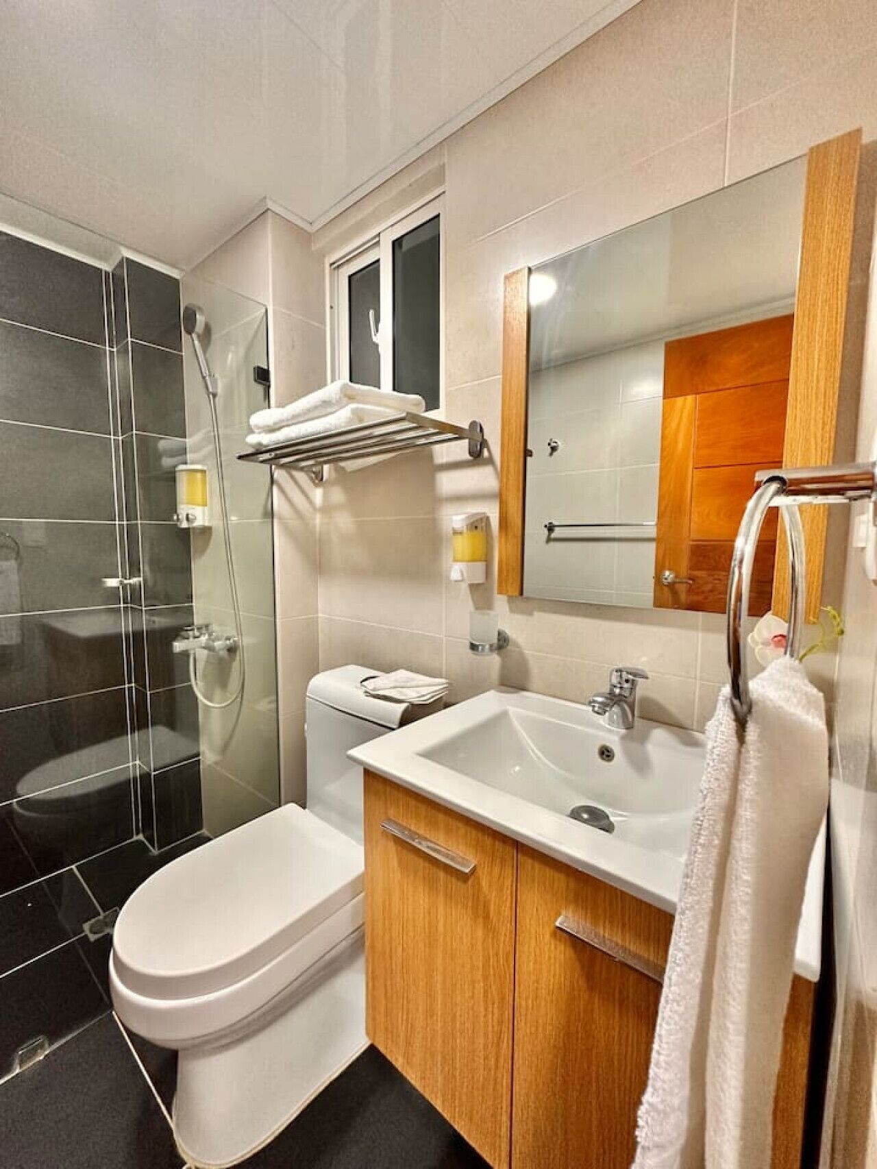 A modern bathroom with a glass-enclosed shower, a white toilet, a wooden vanity with a sink, and a mirror with a wooden frame.