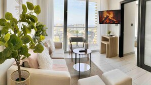 Ein modernes Wohnzimmer mit einer Couch, einem Couchtisch, einem Fernseher und einem Balkon mit Blick auf die Stadt.