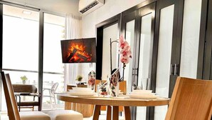 Ein moderner Essbereich mit einem runden Holztisch, vier gepolsterten Stühlen, einem Deckenventilator und einem Fernseher, der ein Feuer zeigt.