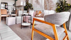 Ein modernes Wohnzimmer mit einer Couch, einem Couchtisch und Sesseln, im Hintergrund eine Küche und große abstrakte Wandbilder.