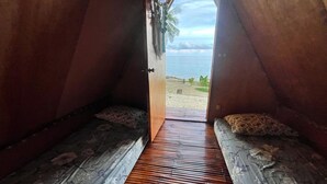 Un dormitorio en el ático con suelo de madera, dos camas con ropa de cama estampada y vistas a la playa a través de una puerta abierta.