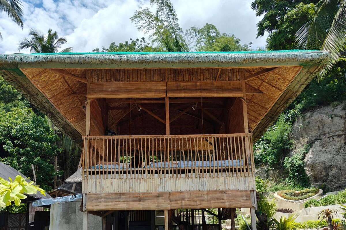 Une structure en bois dotée d’un balcon, entourée d’un jardin avec un chemin de gravier.