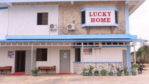 A building with a sign reading "LUCKY HOME" and a small entrance with a red carpet. - Lucky Home Hotel and Apartment (Tinian)