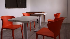 A room with a white table, four orange chairs, and a black-framed window. - Lucky Home Hotel and Apartment (Tinian)