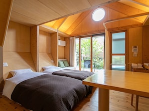 A wooden cabin with two beds, a table, and a large window.