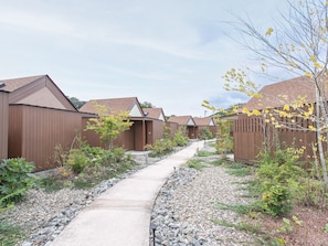 A row of wooden cabins with a gravel path leading through a landscaped garden.