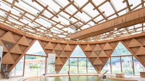 Un balneario de madera tradicional con una fuente termal central, vigas de madera y ventanas amplias.
