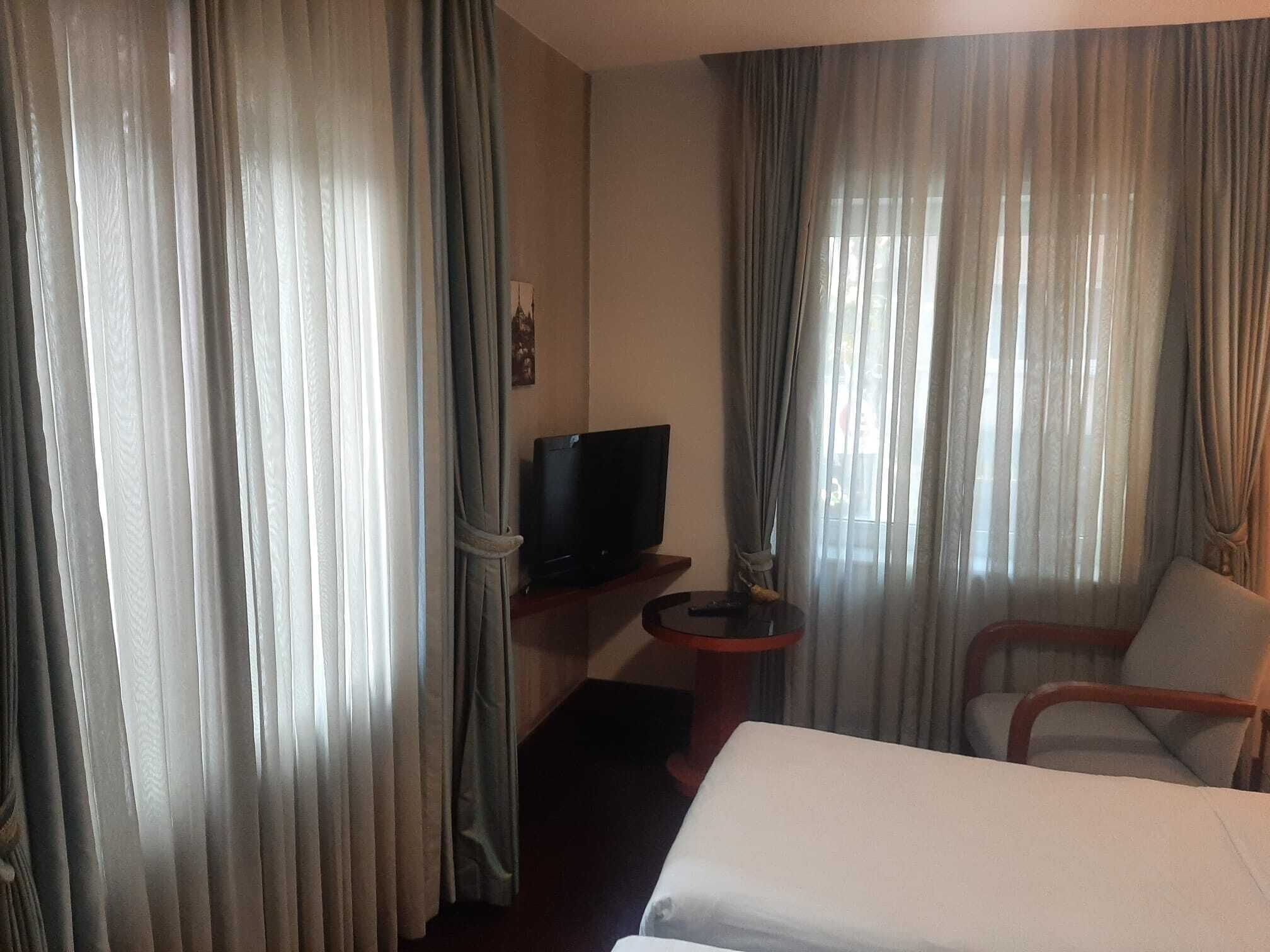A hotel room with a bed, a TV on a stand, a chair, and curtains.