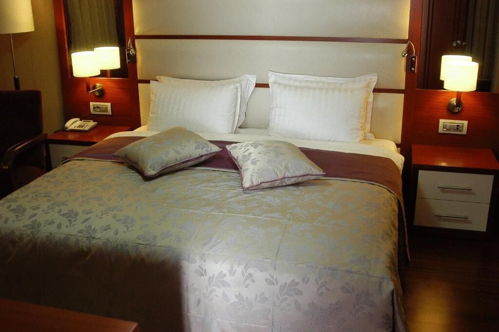 A hotel room with a large bed, two bedside tables, a nightstand, and a lamp on each side.