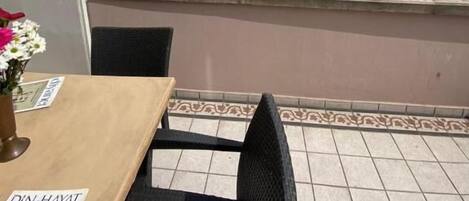 A rooftop terrace with a table and chairs, a flag, and buildings in the background.