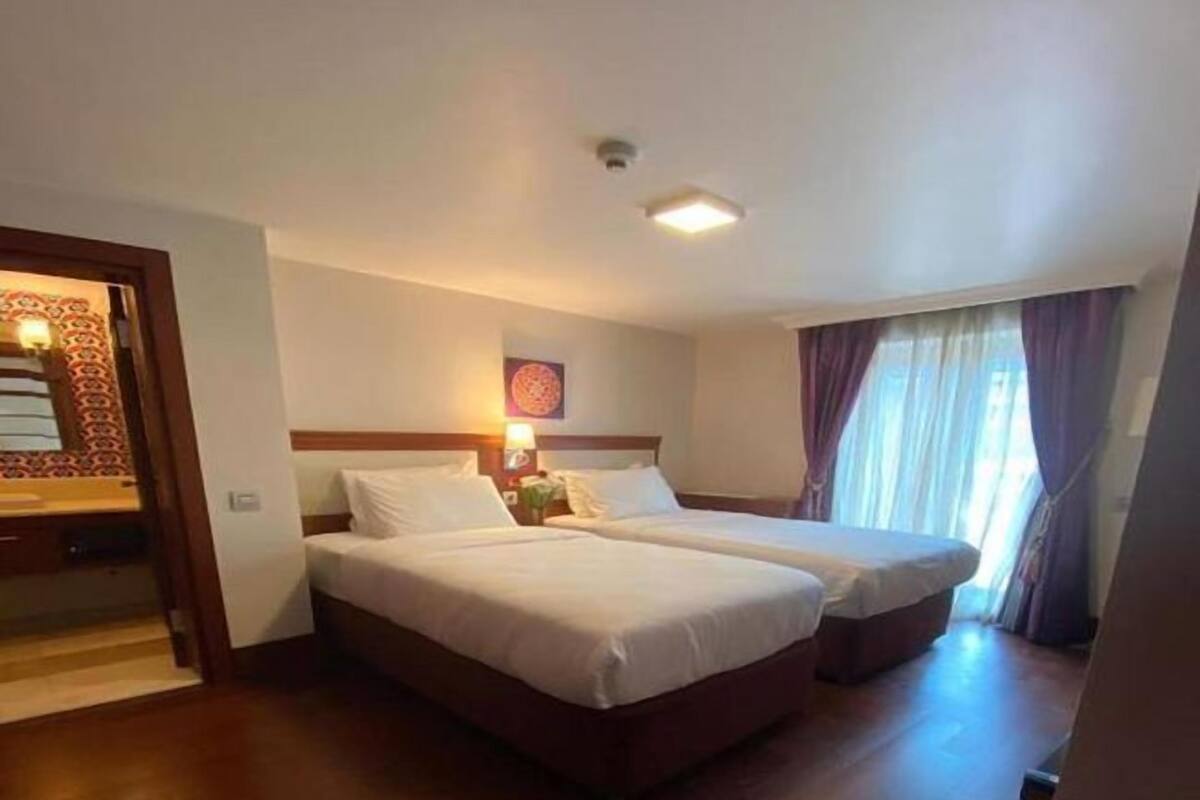 A hotel room with two beds, a wooden floor, a ceiling light, and a door with a patterned design.