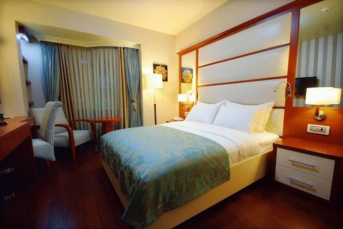 A hotel room with a bed, a desk, a chair, a nightstand, and a mirror.