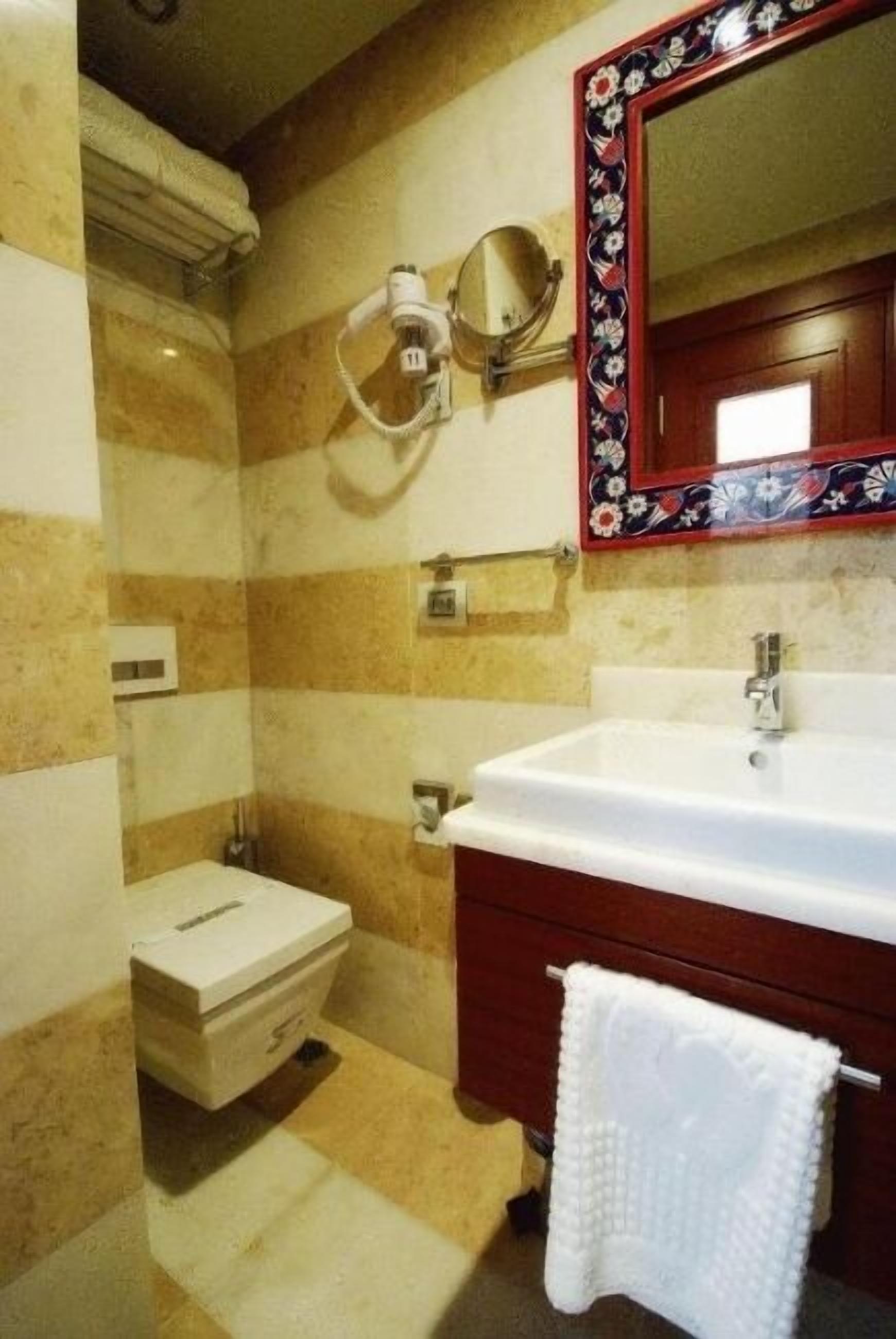 A bathroom with a white sink, a mirror with a floral frame, and a towel hanging on a rack.