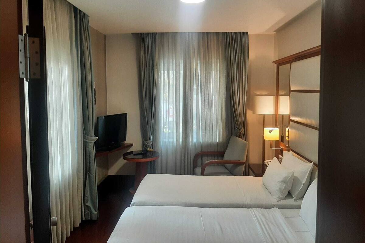 A hotel room with a bed, a TV, a chair, a desk, and a lamp.