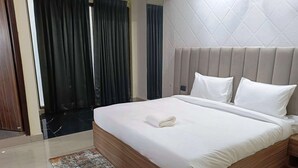 A hotel room with a large bed, a wooden headboard, a small bedside table, and a patterned rug. - Pacific Inn City Center (Gurugram)