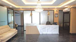 A reception area with a marble counter, a chandelier, and a sofa. - Pacific Inn City Center (Gurugram)