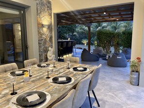 An outdoor dining area with a stone wall, a pergola, and a view of palm trees. - Villa Contemporaine - Côte Ouest (Rivière Noire)