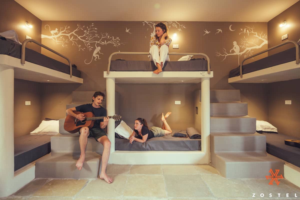 A dormitory room with bunk beds, a staircase, and a mural on the wall.