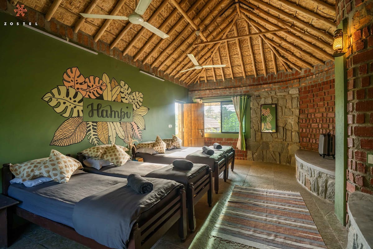A room with two beds, a stone wall, a thatched roof, and a green wall with leaf patterns.