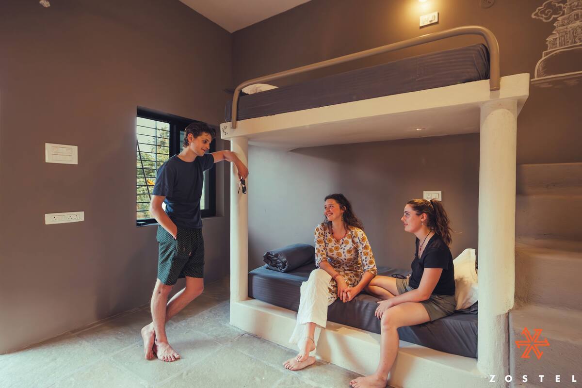 A bunk bed room with a window, a wall socket, and a wall-mounted light fixture.