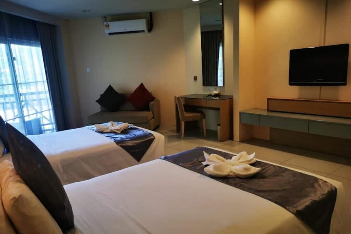 A hotel room with two beds, a desk, a chair, a television, and a large window.