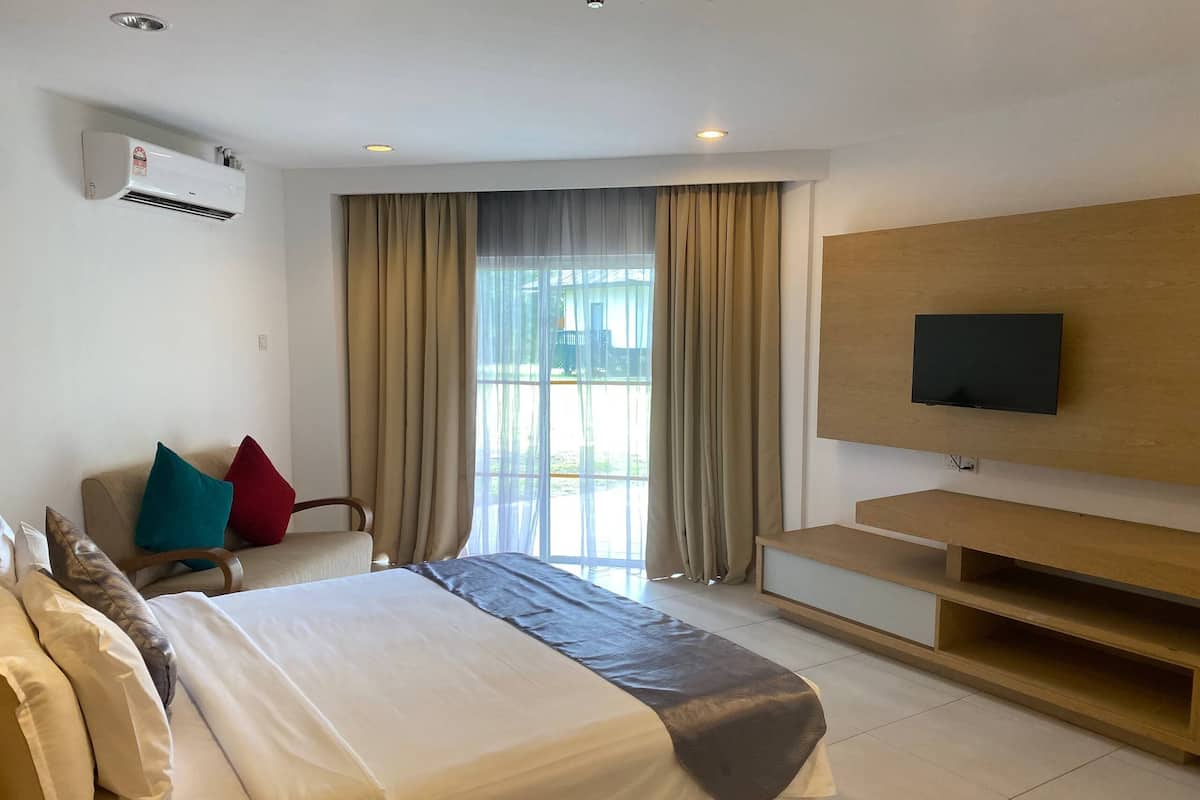 A hotel room with a bed, a TV, a desk, and a window with curtains.