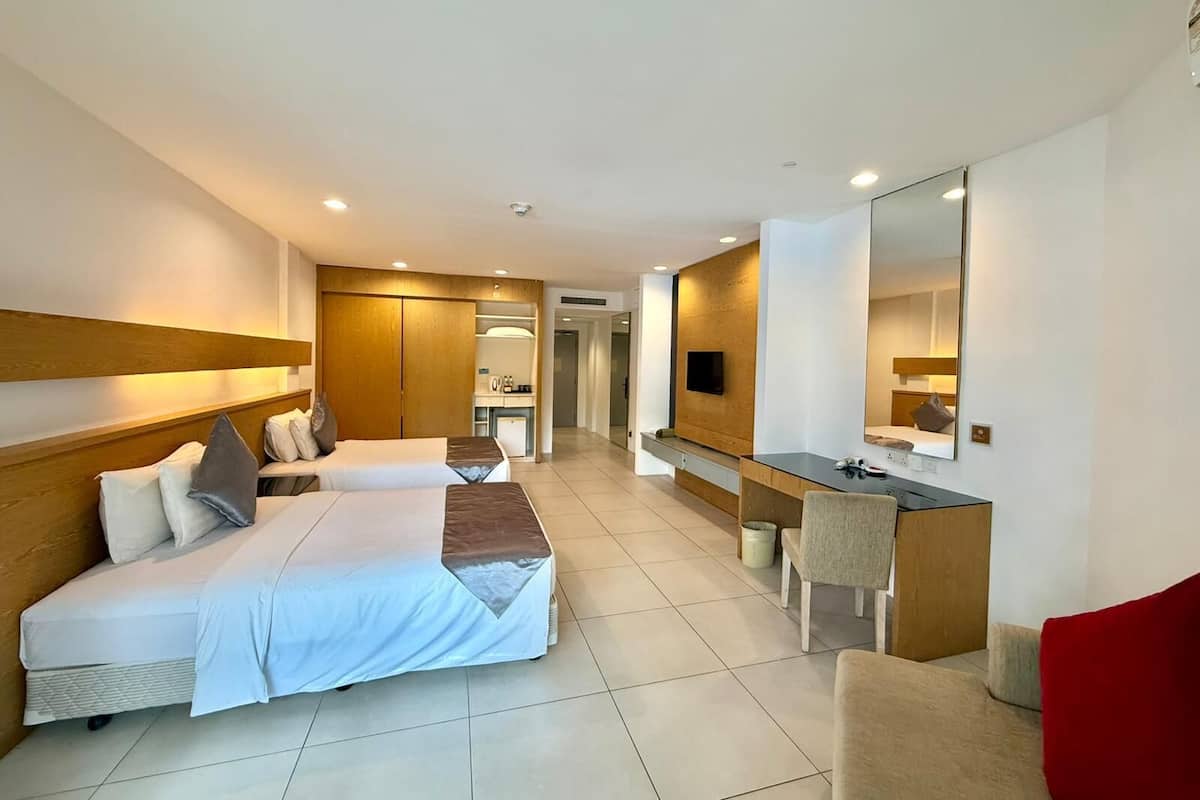 A hotel room with two beds, a desk, a mirror, and a TV.