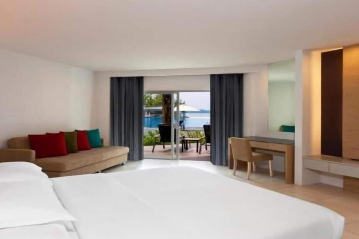 A hotel room with a bed, a sofa with colorful cushions, a desk, and a TV.
