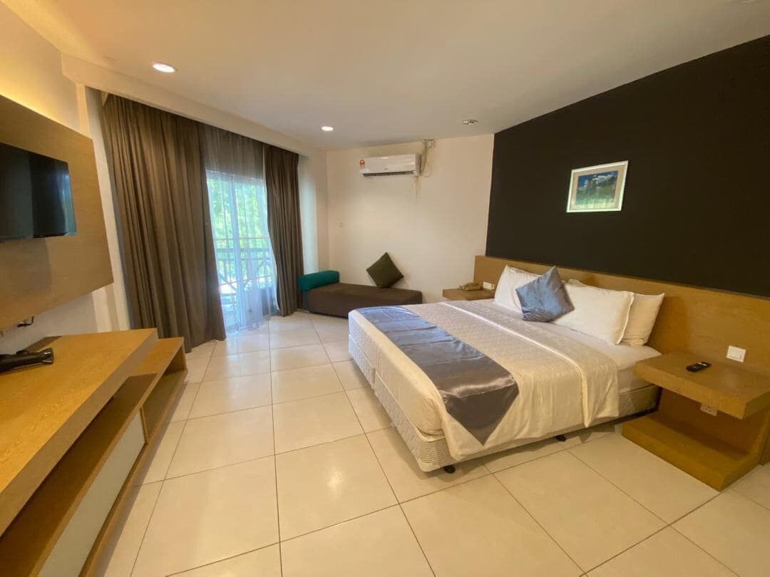 A hotel room with a bed, a TV, a desk, a chair, and a window with curtains.