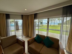 A room with a sofa and armchairs, large windows with curtains, and a view of a grassy area and water. - Century Langkasuka Resort Langkawi (Langkawi)