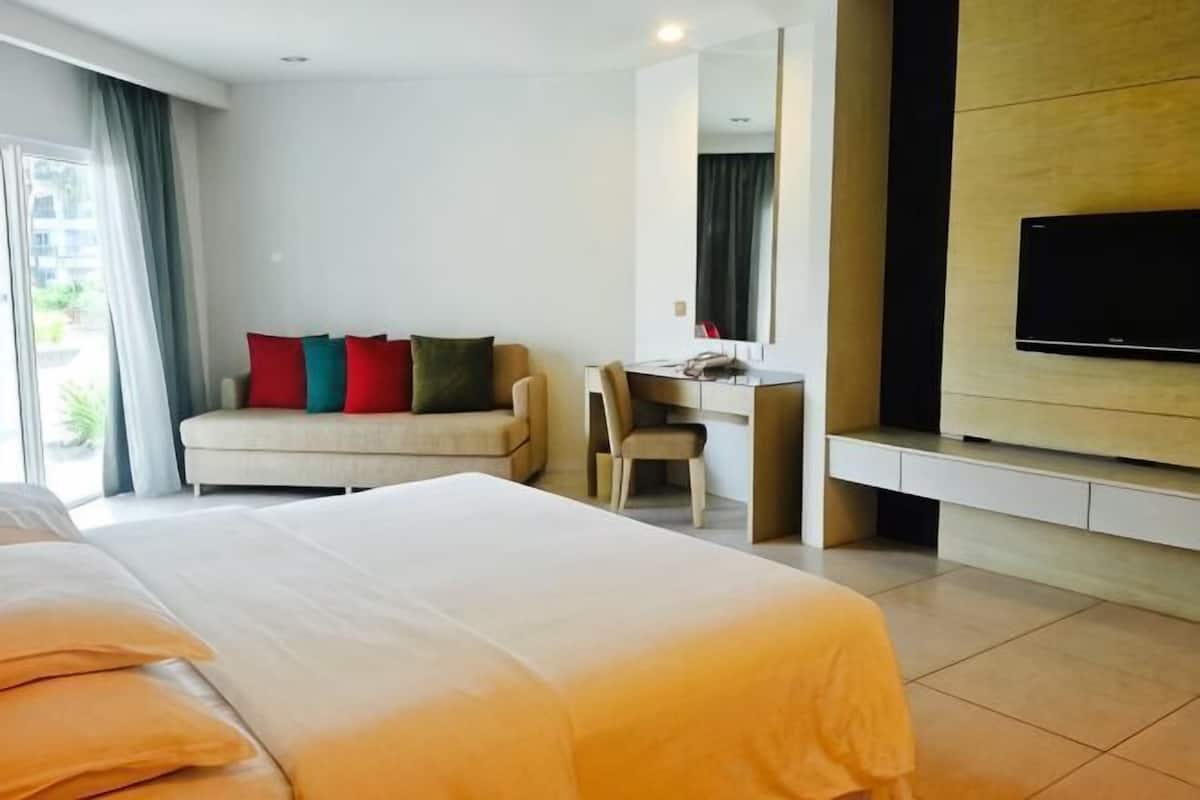 A hotel room with a bed, a desk, a sofa, and a TV mounted on the wall.