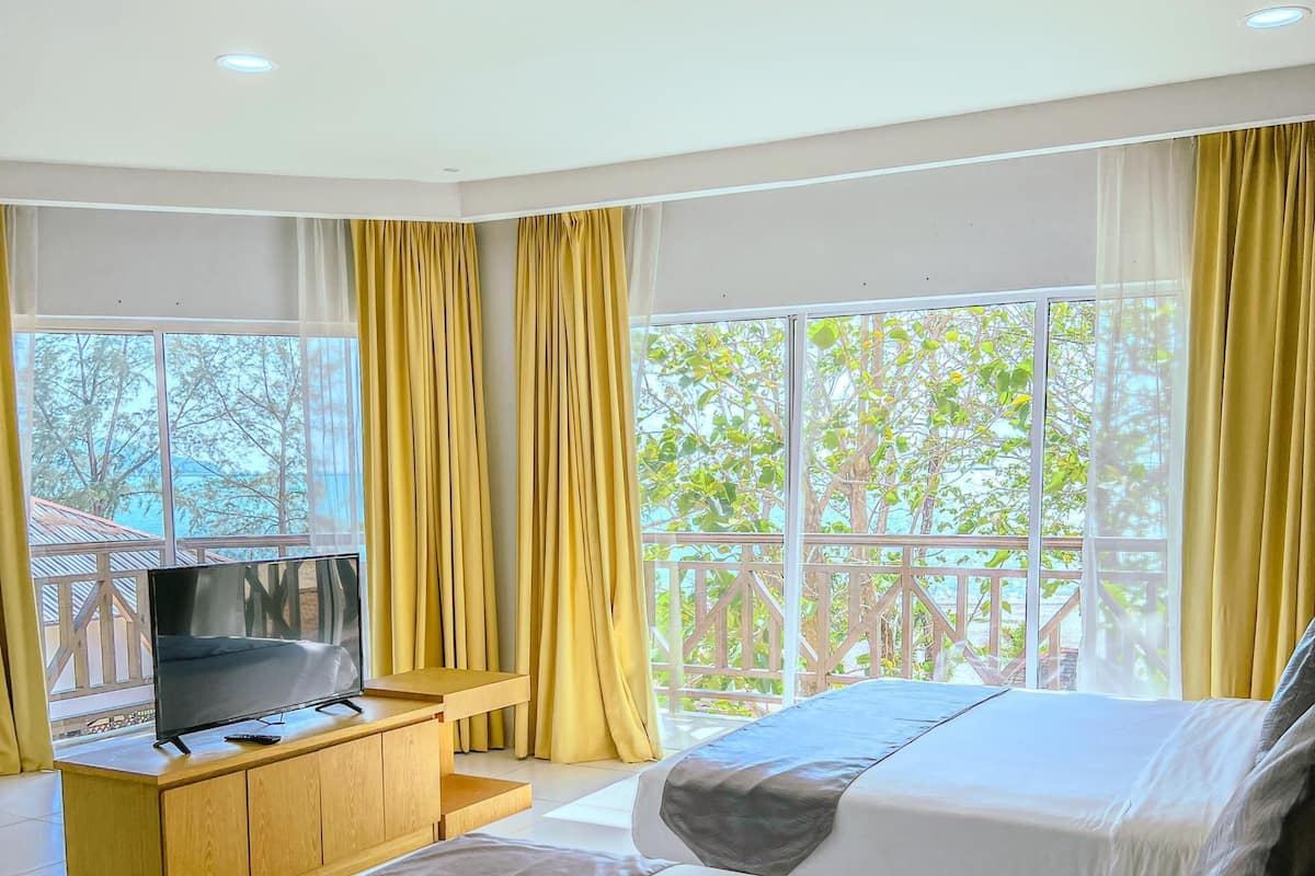 A hotel room with two beds, a TV on a wooden cabinet, and large windows with curtains.
