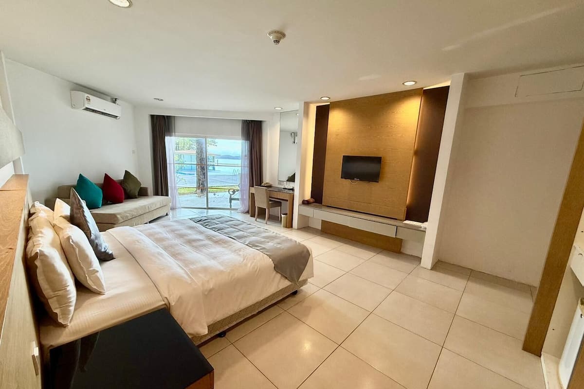 A modern hotel room with a large bed, a desk, a flat-screen TV mounted on a wooden panel, and a view of the outdoors.