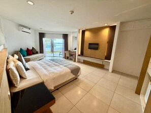 A modern hotel room with a large bed, a desk, a flat-screen TV mounted on a wooden panel, and a view of the outdoors. - Century Langkasuka Resort Langkawi (Langkawi)